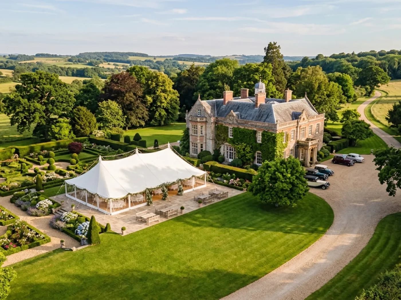 Aerial photograph of a country house wedding venue with a marquee lawn and formal gardens laid out below